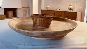 Une table à manger sur laquelle se trouvent un grand saladier en bois et un panier tressé.