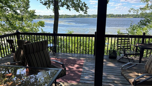 Une terrasse avec des sièges extérieurs, une table en verre et une vue sur un lac.