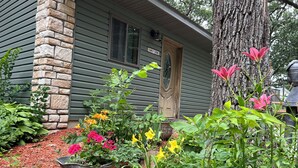 Un chalet rustique avec une façade en pierre, une porte en bois et un jardin agrémenté de diverses plantes et fleurs.