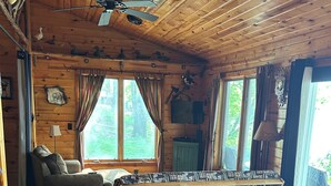 L’intérieur d’un chalet en bois, avec un canapé, un banc, une table à manger et un ventilateur de plafond.