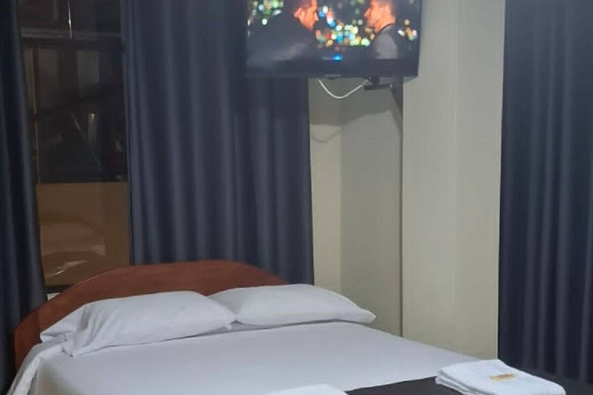 Hotellihuone, jossa on sänky, seinälle asennettu taulutelevisio ja ikkuna, jossa on verhot.