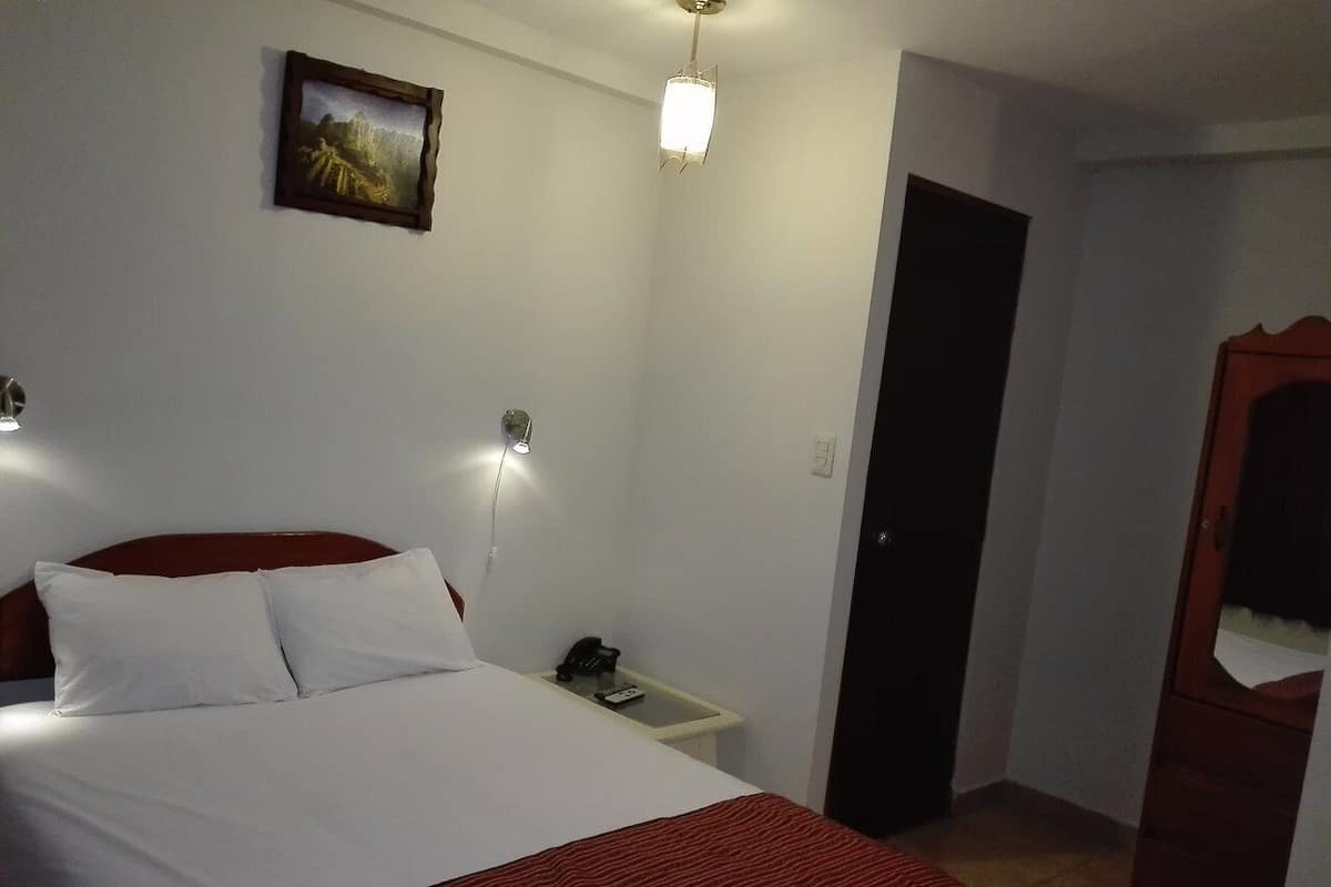 Hotellihuone, jossa on sänky, yöpöytä, lamppu ja ovi.