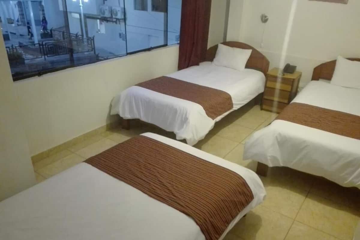 Hotellihuone, jossa on kolme erillistä sänkyä, suuri ikkuna ja näkymä kadulle.