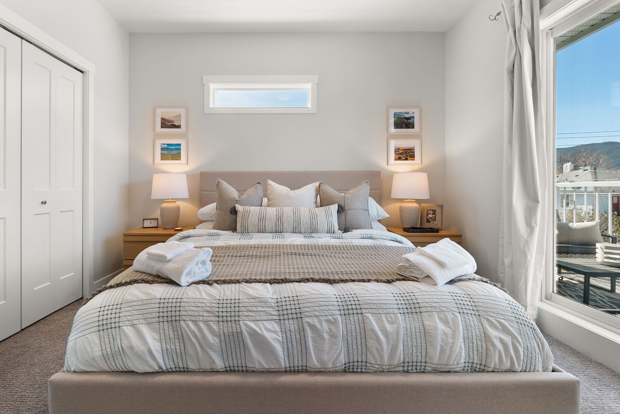 A neatly made bed with a checkered comforter and multiple pillows, two bedside lamps, and framed pictures on the nightstands.