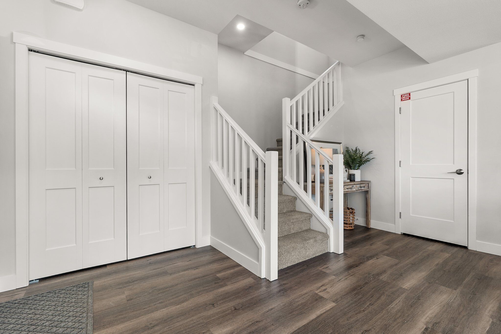 Un couloir propre et moderne, avec un plancher en bois, des portes blanches et un escalier doté de rampes blanches.