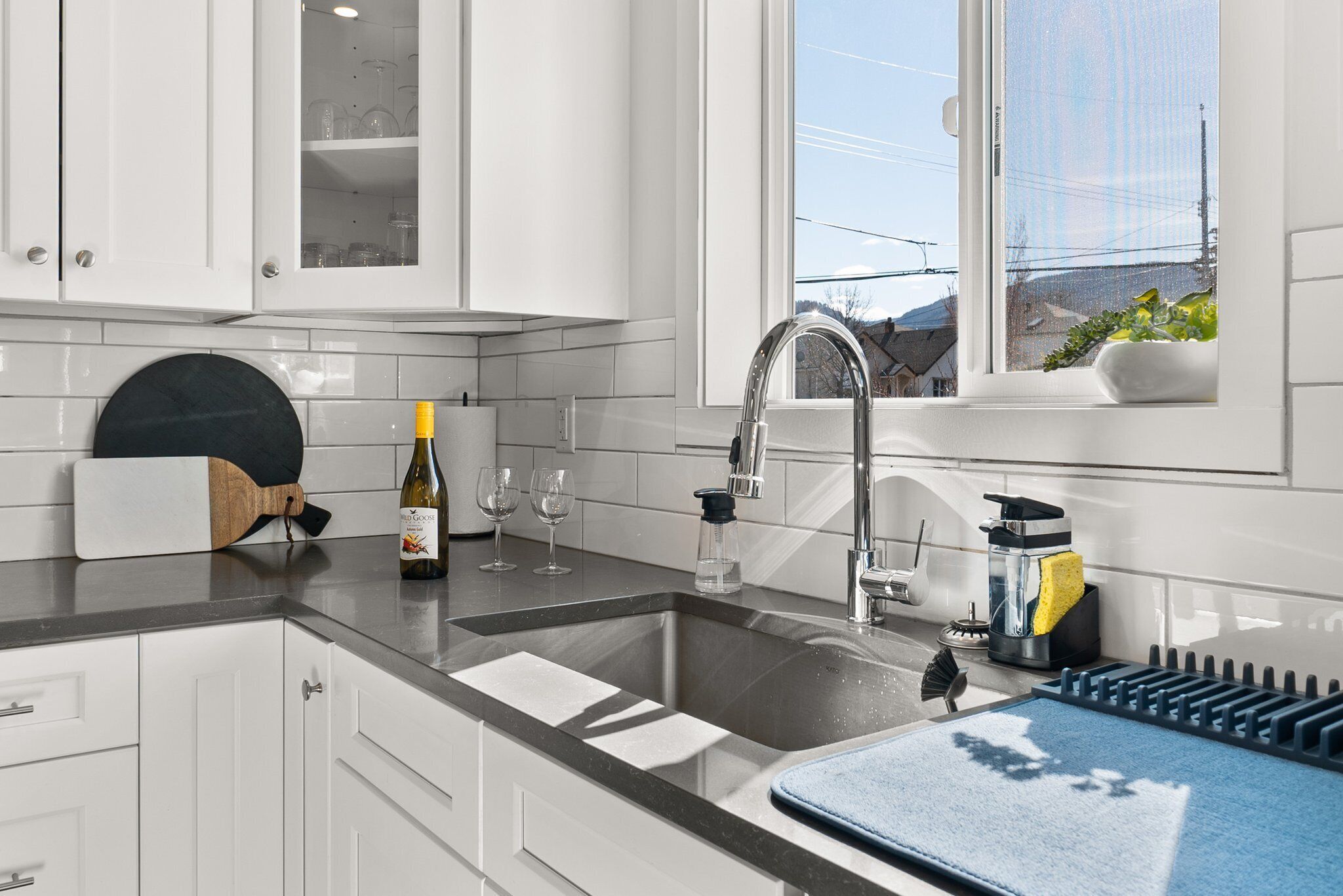 A modern kitchen with white cabinets, a stainless steel sink, and a window with a view of the outside.