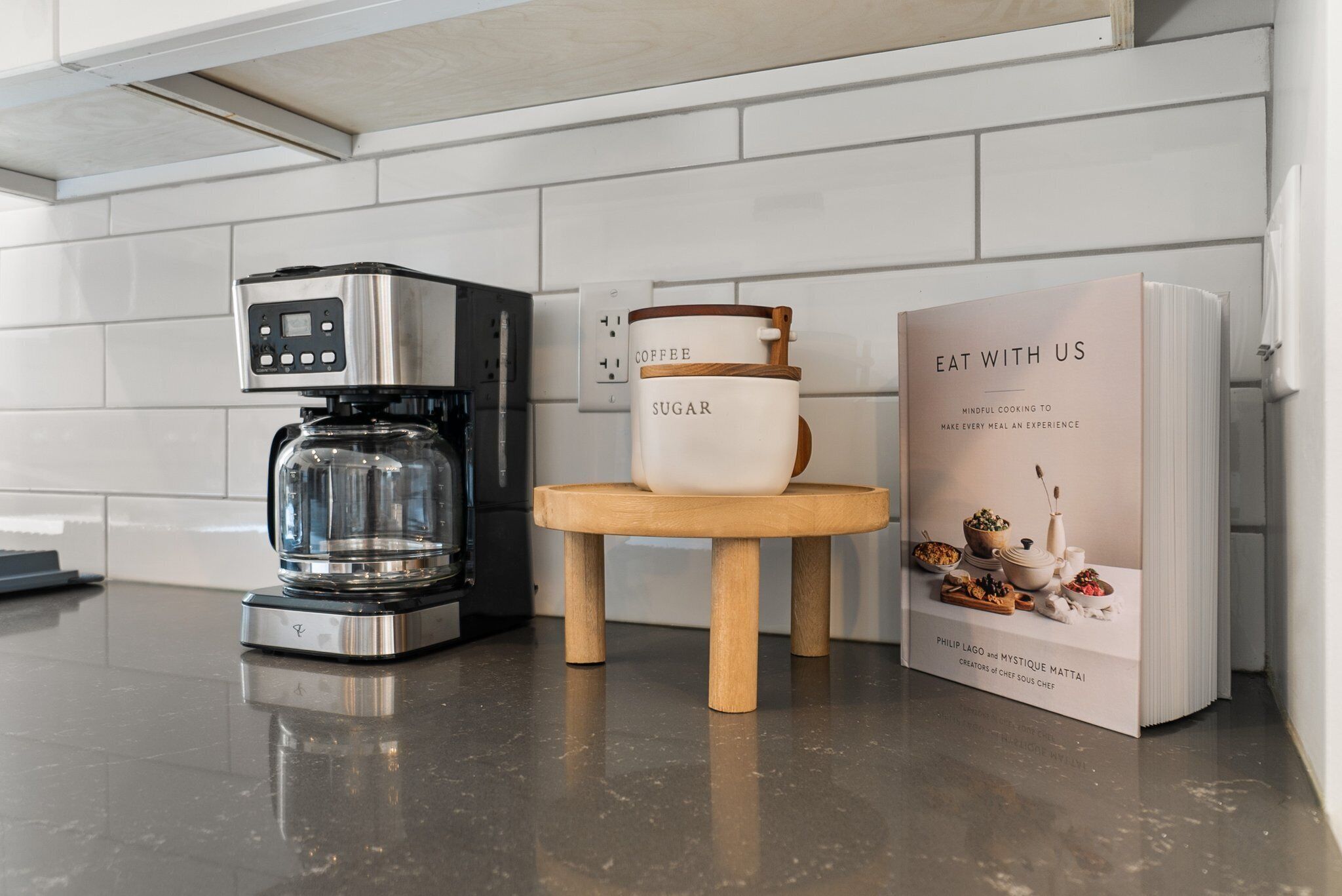 Een moderne keuken met een koffiezetapparaat, een suikerpot en een kookboek op het aanrecht.