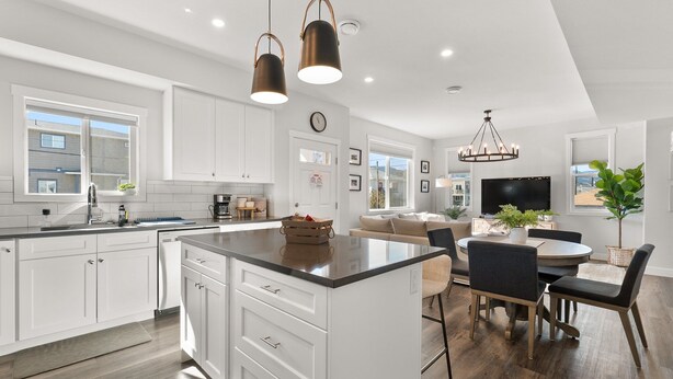 Une cuisine moderne avec des meubles blancs, un îlot central et des luminaires suspendus.