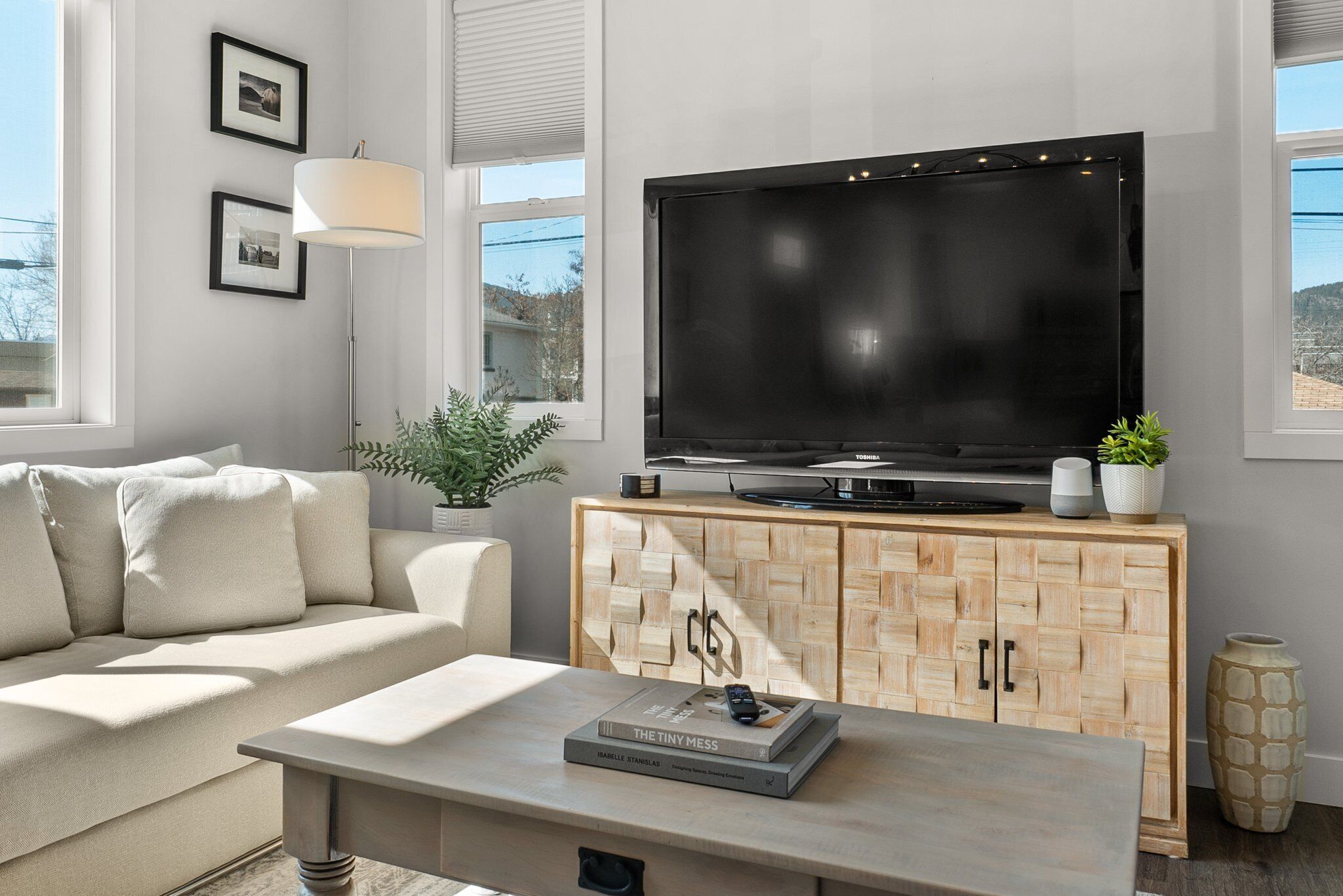 A modern living room with a large flat-screen TV, a light-colored sofa, a wooden cabinet, and a coffee table.