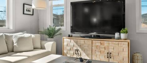 A modern living room with a large flat-screen TV, a light-colored sofa, a wooden cabinet, and a coffee table.