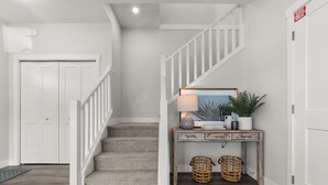 Un escalier avec une rampe blanche menant à un palier où se trouvent un bureau, une lampe et des paniers en osier.