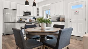 Une cuisine moderne avec des meubles blancs, des appareils en acier inoxydable, une table de salle à manger ronde avec des chaises et des luminaires suspendus.