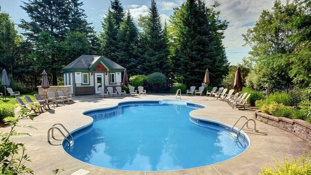 A swimming pool with lounge chairs and a small building in the background. - Golf Course Townhome with Deck, BBQ & Views – 4BR Mont Tremblant (Mont-Tremblant)