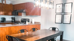 A modern kitchen with wooden cabinets, a central island, and a dining area with a large wooden table and chairs. - Golf Course Townhome with Deck, BBQ & Views – 4BR Mont Tremblant (Mont-Tremblant)