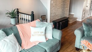 A modern living room with a grey sofa, a coffee table with flowers, a staircase, and a stone wall. - Golf Course Townhome with Deck, BBQ & Views – 4BR Mont Tremblant (Mont-Tremblant)