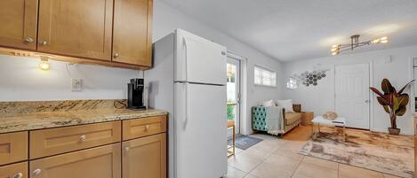 A kitchen with wooden cabinets, a white refrigerator, a coffee maker, and a dining area with a sofa and table.