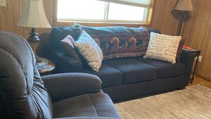 Een gezellige woonkamer met een donkergrijze bank, een bijpassende fauteuil en een gebreid plaid.