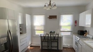 A kitchen with white cabinets, a stainless steel refrigerator, a gas stove, and a dining area with two chairs. - Wineries, Hiking, skiing  and fishing minutes from house (Saylorsburg)