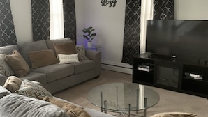 A modern living room with a grey sofa, a glass coffee table, a ceiling fan, and a flat-screen TV. - Wineries, Hiking, skiing  and fishing minutes from house (Saylorsburg)