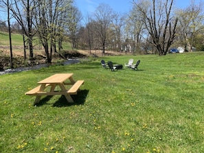A picnic area with a wooden table and chairs, surrounded by grass and trees.