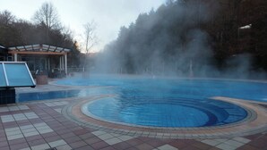 A swimming pool with a tiled deck and a covered area with a bench.
