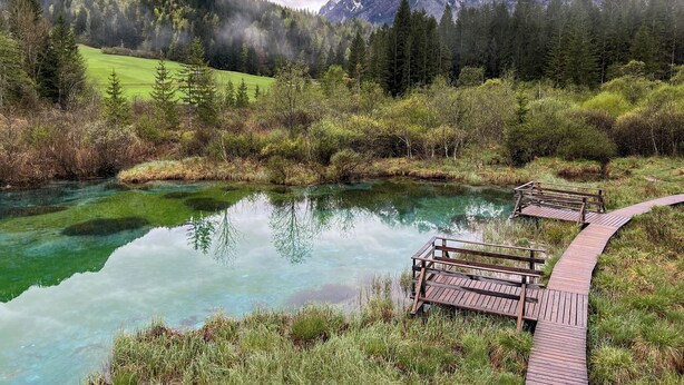 A clear mountain lake with wooden walkways and a forested mountain backdrop.