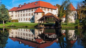 A large building with a red roof, a pond in front, and a wooden structure on the pond.