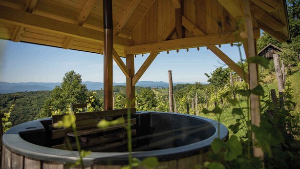 Een houten gazebo met een jacuzzi, omgeven door weelderige begroeiing en een prachtig uitzicht op verre bergen.