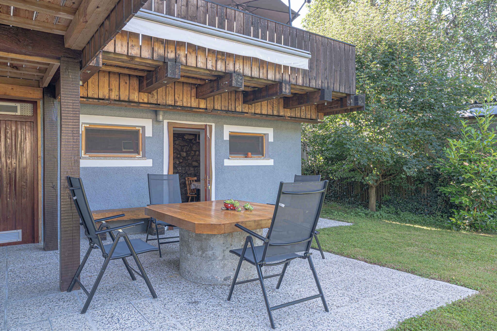 An outdoor dining area with a concrete table and metal chairs, set against a building with wooden balconies and a stone wall.