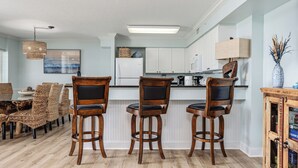 A kitchen with white cabinets, a white refrigerator, a wooden bar stool, and a hanging light fixture.