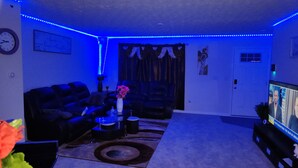 A living room with a sofa, coffee table, and a TV. Blue LED lights line the ceiling. - Ryan Home (Columbus)