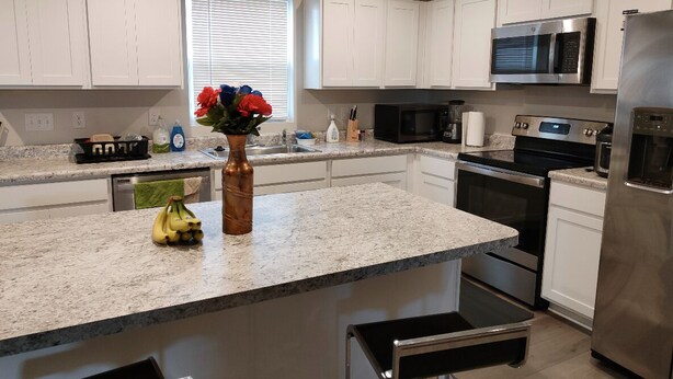 A modern kitchen with white cabinets, a granite countertop, stainless steel appliances, and a vase with flowers. - Ryan Home (Columbus)