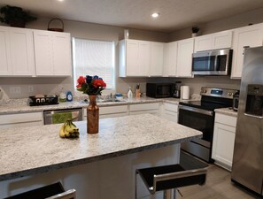 Una cocina moderna con armarios blancos, encimera de granito, electrodomésticos de acero inoxidable y un jarrón con flores.