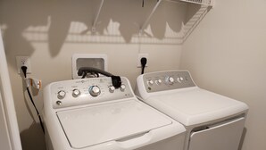 A laundry area with a front-loading washer and dryer, a power outlet, and a shelf above the dryer. - Ryan Home (Columbus)