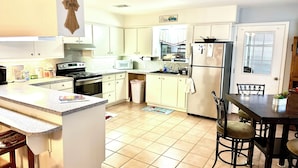 A kitchen with white cabinets, a stove, microwave, and a refrigerator. There is a dining table with chairs and a small potted plant. - Riverfront Home w/kayaks, firepit, grill, fish 8mi Coopers 8mi Castell Gen Store (Llano)