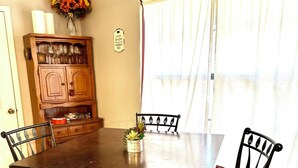 A dining area with a wooden table and four chairs, a cabinet with glassware, and a window with curtains. - Riverfront Home w/kayaks, firepit, grill, fish 8mi Coopers 8mi Castell Gen Store (Llano)