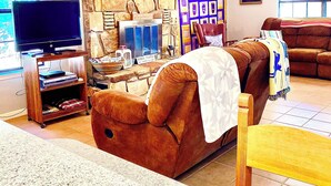 A living room with a stone fireplace, a television, a bookshelf, and a large window. - Riverfront Home w/kayaks, firepit, grill, fish 8mi Coopers 8mi Castell Gen Store (Llano)