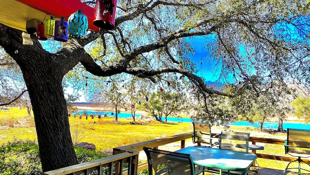 A wooden deck with outdoor seating, a large tree, and colorful hanging lanterns. - Riverfront Home w/kayaks, firepit, grill, fish 8mi Coopers 8mi Castell Gen Store (Llano)