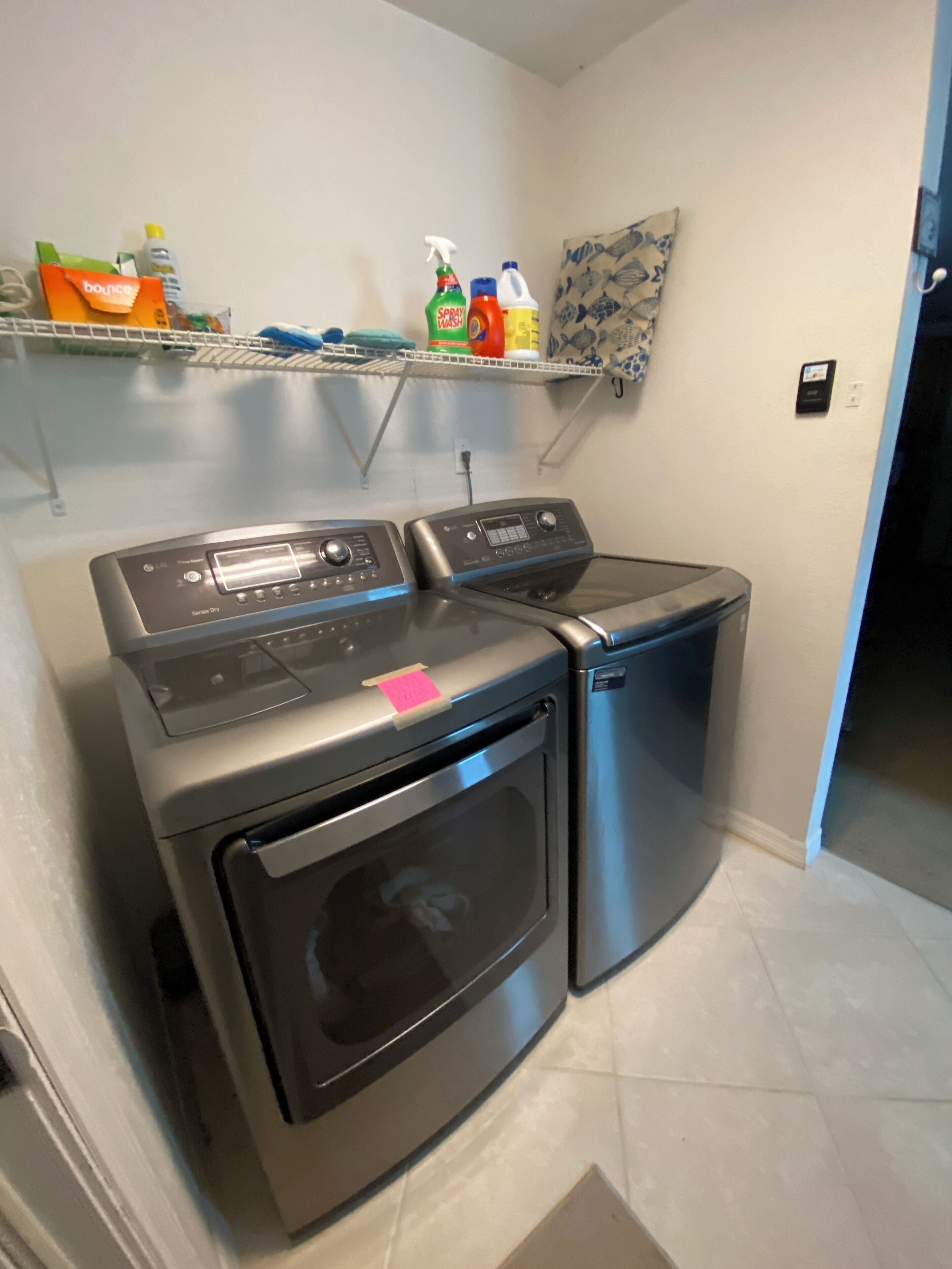 A laundry room with two front-loading washing machines and a shelf above containing cleaning supplies.