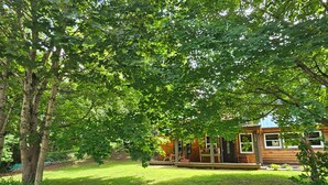 A wooden cabin with a porch, surrounded by lush greenery and trees. - 2 STORY ADIRONDACK LOG CABIN-SKI ! SKI! SKI! (Lake George)