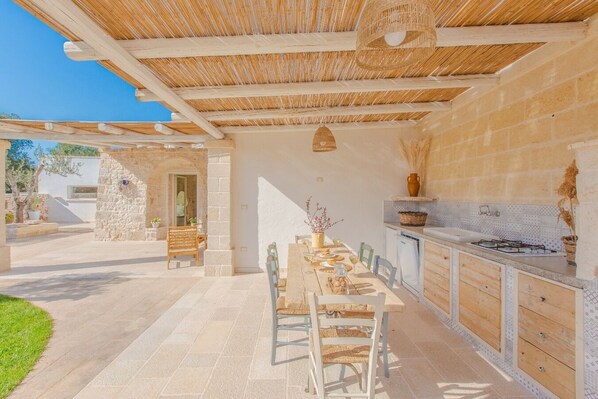 An outdoor patio with a dining table, chairs, and a kitchen area with a stove and cabinets.