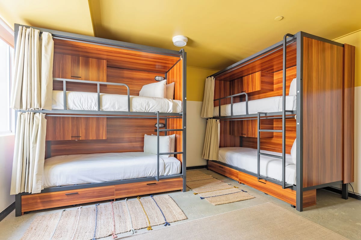 A bunk bed room with wooden headboards, a small window with curtains, and a light fixture on the ceiling.