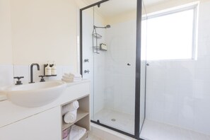 A modern bathroom with a white sink, vanity, and a glass-enclosed shower. - Roamer Brisbane (Brisbane)
