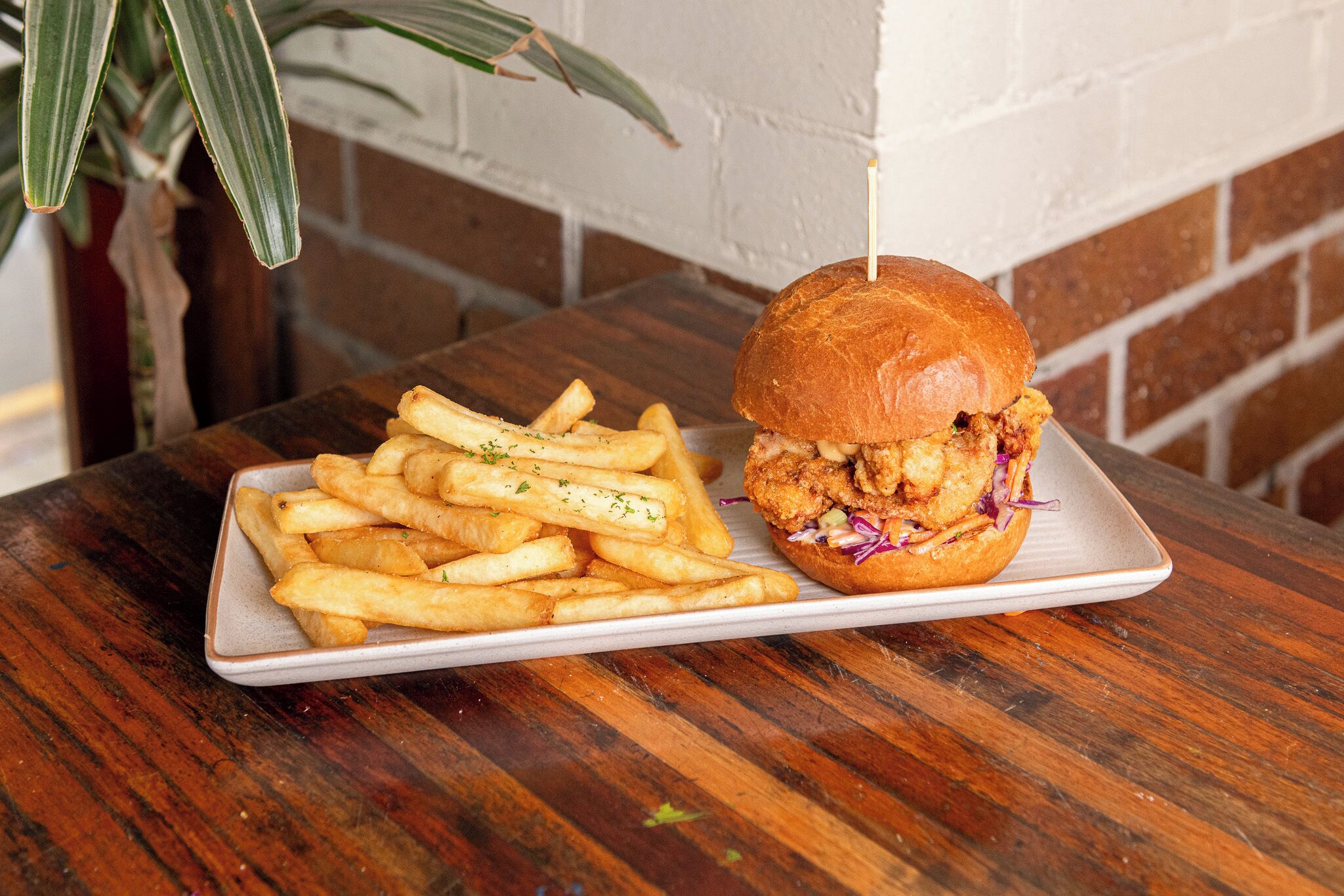 Une assiette contenant un sandwich au poulet et des frites, posée sur une table en bois.
