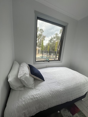 A bedroom with a bed, pillows, a window, and a view of trees and a fence. - The Cutting Estate Mount Panorama (Mount Panorama)