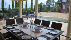 A dining area with a table set for six, outdoor chairs, and a view of a swimming pool and garden. - The Cutting Estate Mount Panorama (Mount Panorama)