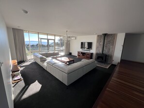 A modern living room with a large sectional sofa, a flat-screen TV, and a stone fireplace. - The Cutting Estate Mount Panorama (Mount Panorama)