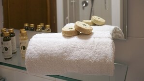 Et badeværelse med et hvidt håndklæde på en glashylde, et spejl og flere toiletartikler.