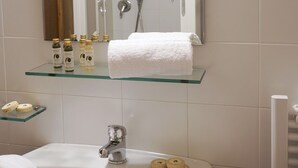 Et badeværelse med en glashyld, toiletartikler, et hvidt håndklæde og en vask med armatur.