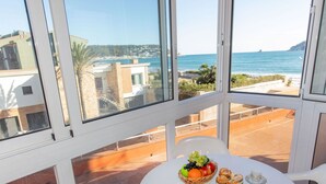 Un balcón con una mesa dispuesta para tomar té, vista al mar y edificios al fondo.